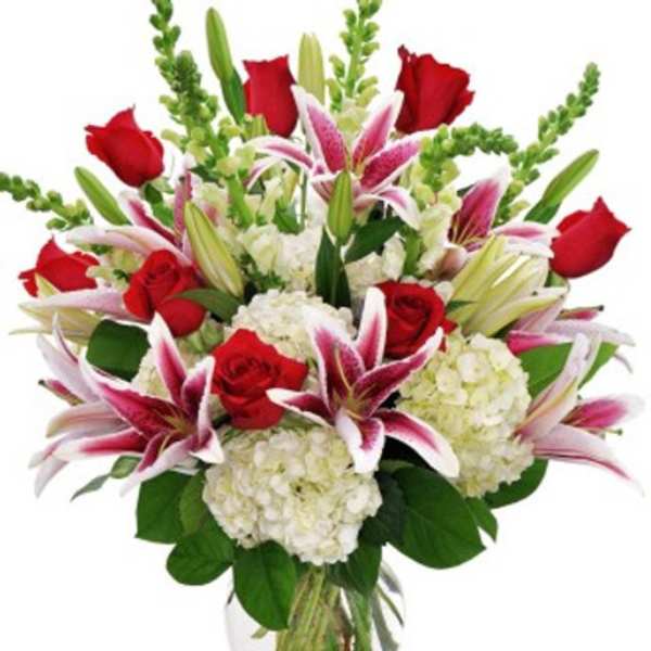 Bouquet of red roses, pink lilies, and white hydrangeas in a glass vase