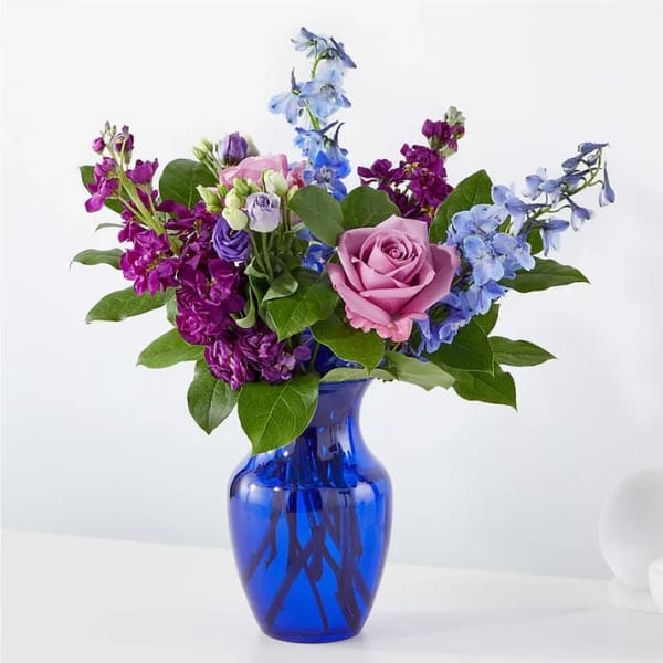Mixed bouquet of pink roses, purple blooms, and blue flowers in a cobalt vase