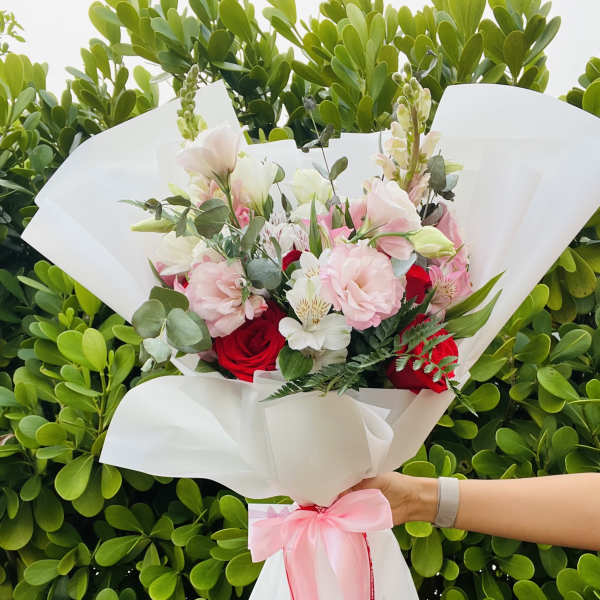 Bouquet of pink and red flowers wrapped in white paper with a pink ribbon