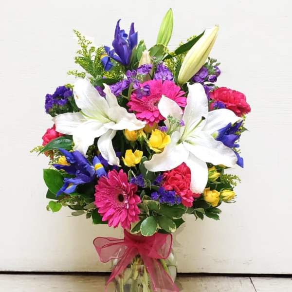 Mixed bouquet with white lilies, pink gerberas, and purple flowers in a glass vase