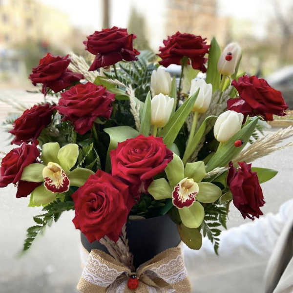 Bouquet of red roses, white tulips, and green orchids in a black vase