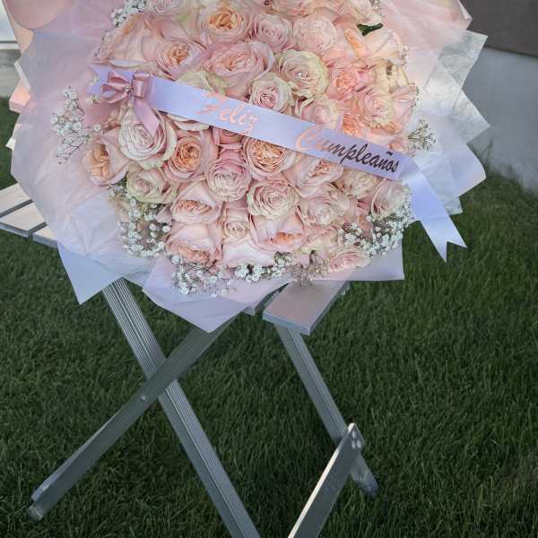 Large bouquet of pale pink roses wrapped in pink paper with a ribbon