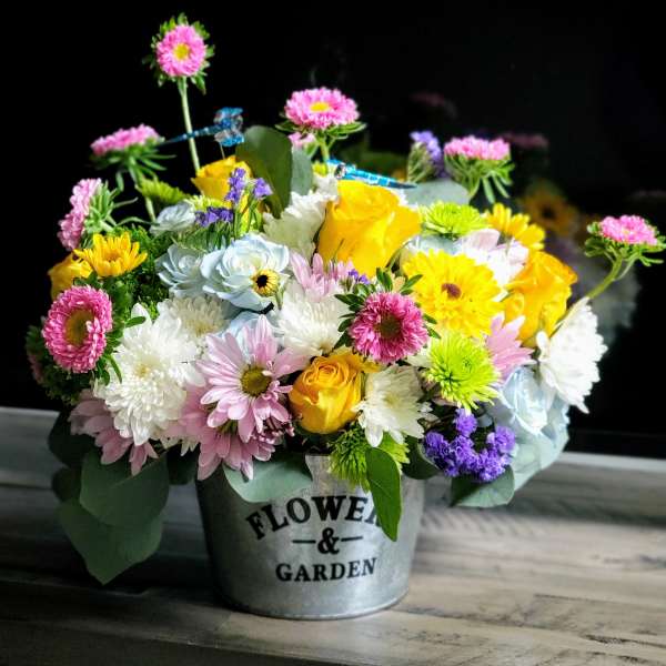 Mixed bouquet of pink, yellow, white, and blue flowers in a metal bucket