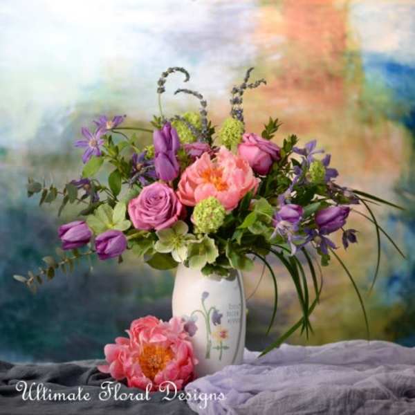 Pink and purple mixed bouquet in a white vase with two loose blooms in front