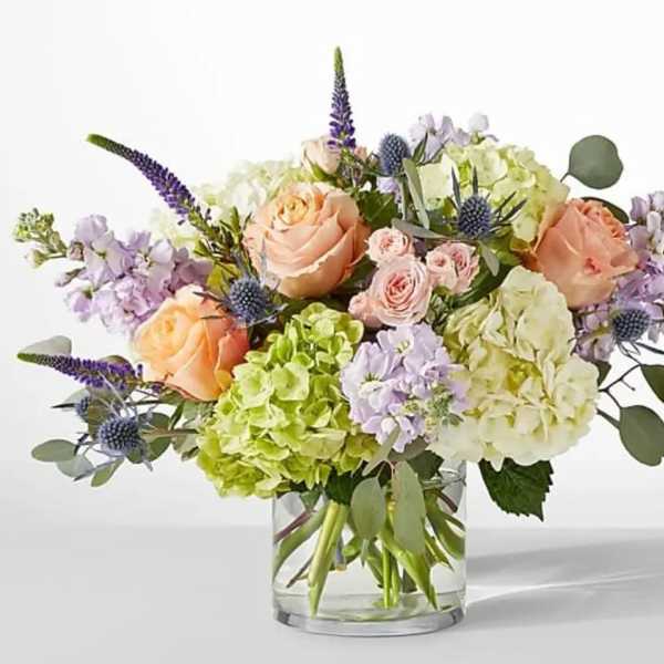 Bouquet of peach roses, hydrangeas, and purple flowers in a glass vase