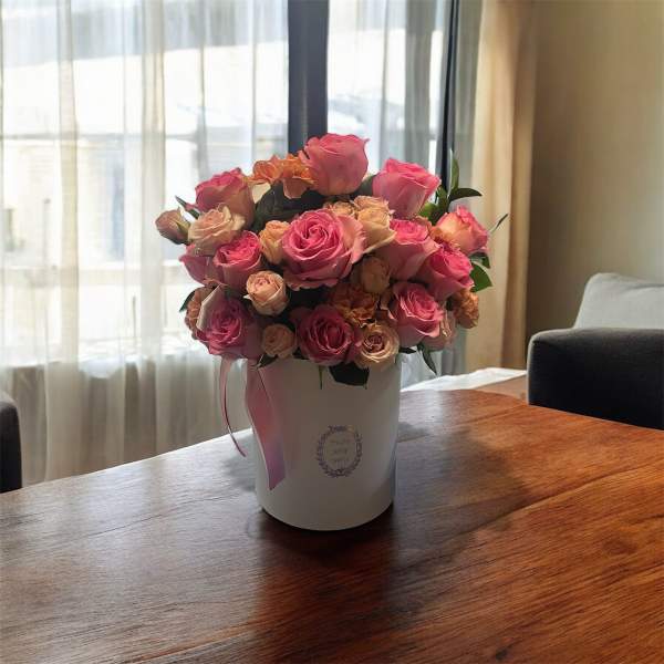 Pink and peach roses arranged in a white hatbox with ribbon