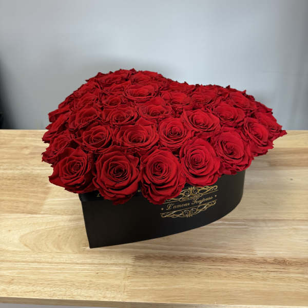 Large red rose arrangement in a black hat box on a wooden table