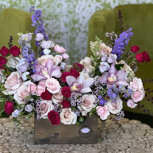 Mixed bouquet of roses, orchids, and purple blooms in a wooden box