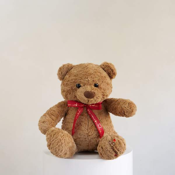 Brown teddy bear with a red ribbon sitting on a white pedestal