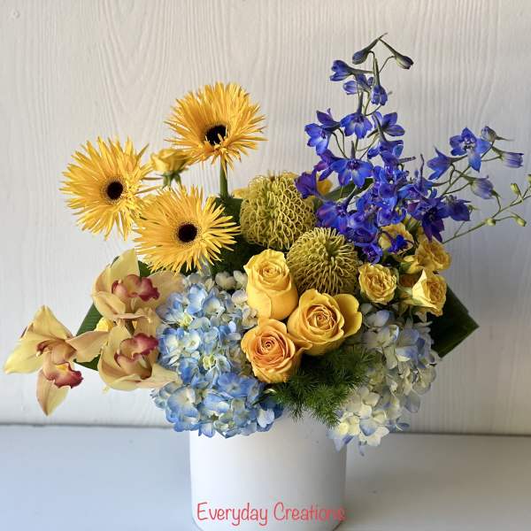 Bouquet of yellow gerbera daisies, blue hydrangeas, and yellow roses in a white vase