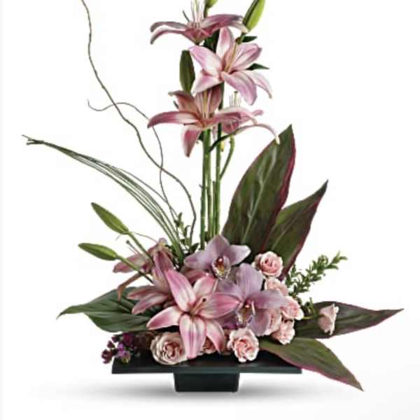 Pink lilies and roses arranged in a low black container with tall stems