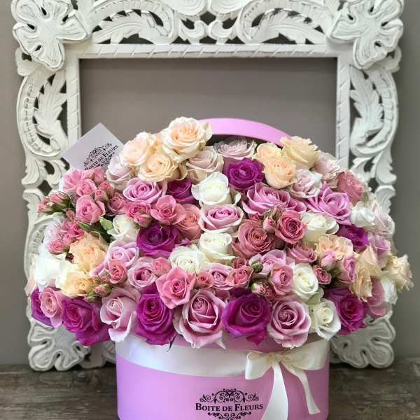 Pink and cream roses arranged in a round hat box with a ribbon
