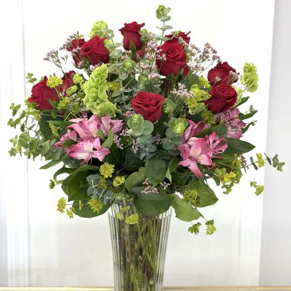 Red roses and pink flowers arranged in a tall glass vase