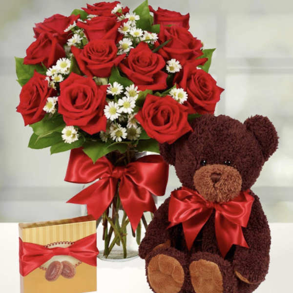 Bouquet of red roses in a glass vase with a teddy bear and chocolate box