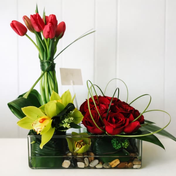 Red tulips and roses arranged in a glass vase with yellow orchids
