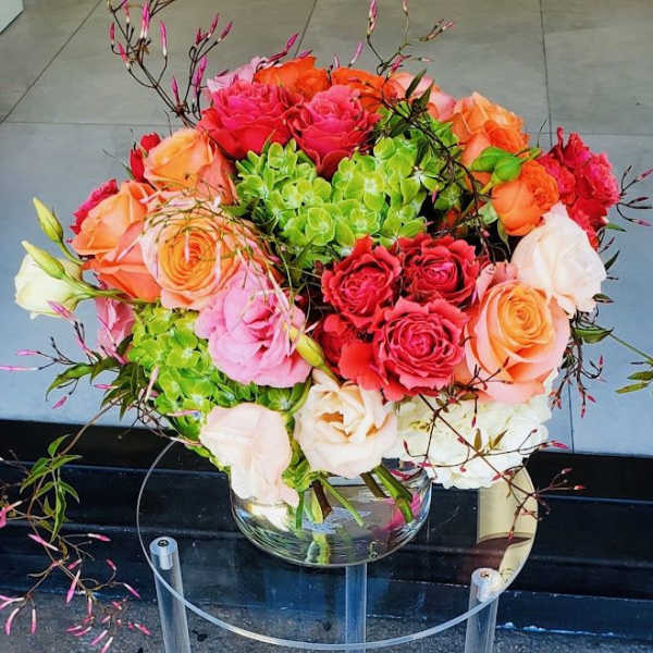 Bright bouquet of orange, pink, and cream roses with green hydrangeas in a clear glass vase