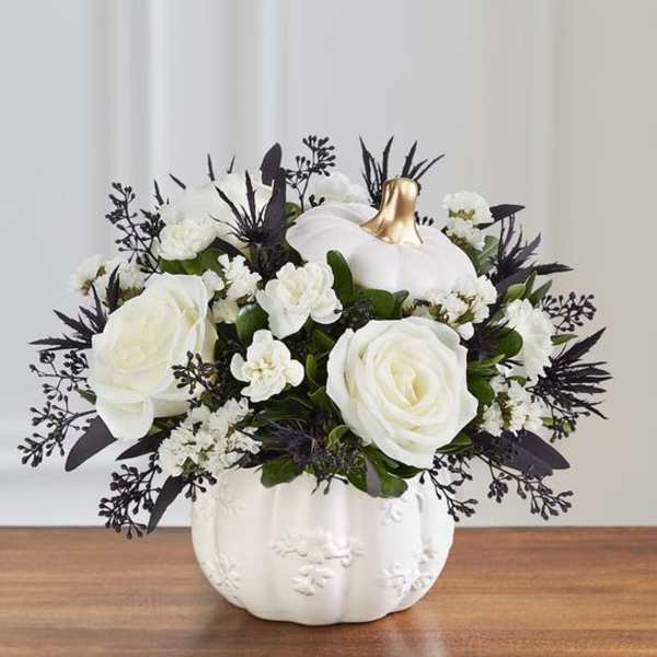 White roses and small white flowers in a white pumpkin vase