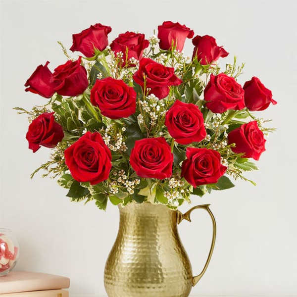 Red roses arranged in a gold pitcher vase