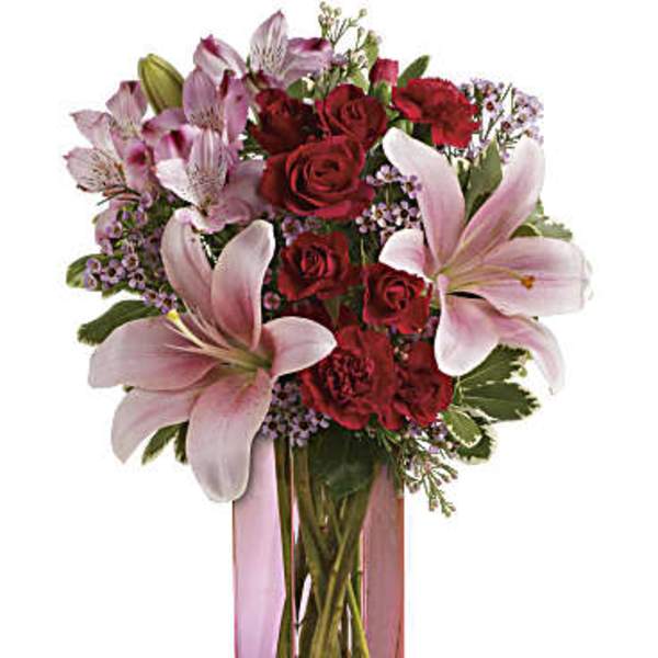 Bouquet of red roses and pink lilies in a tall pink glass vase