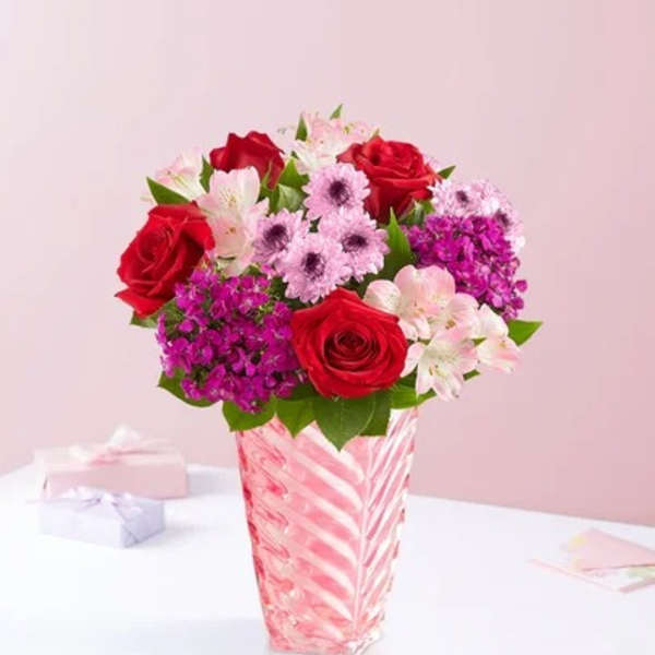 Red roses and pink flowers in a striped glass vase