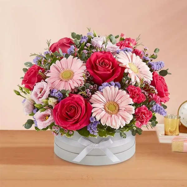 Pink and red roses with pale pink daisies in a round box