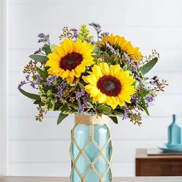 Sunflowers arranged in a blue glass vase with purple filler flowers