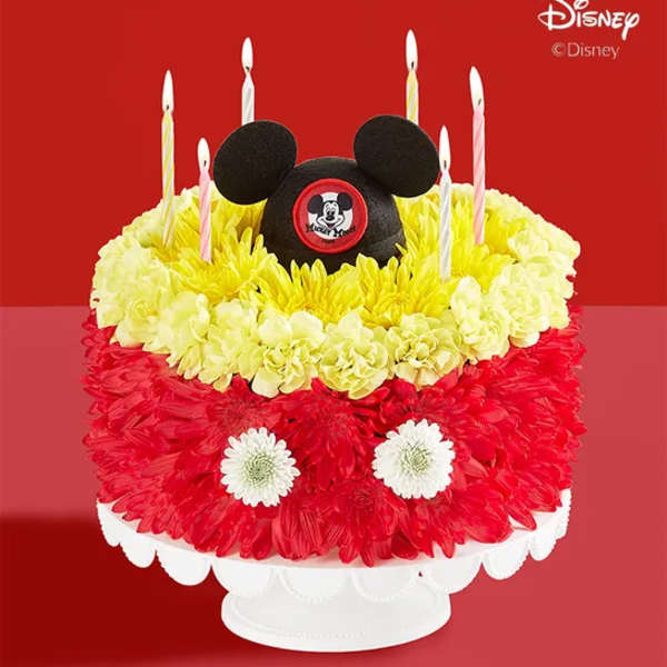 Mickey Mouse-themed floral cake with candles on a white stand