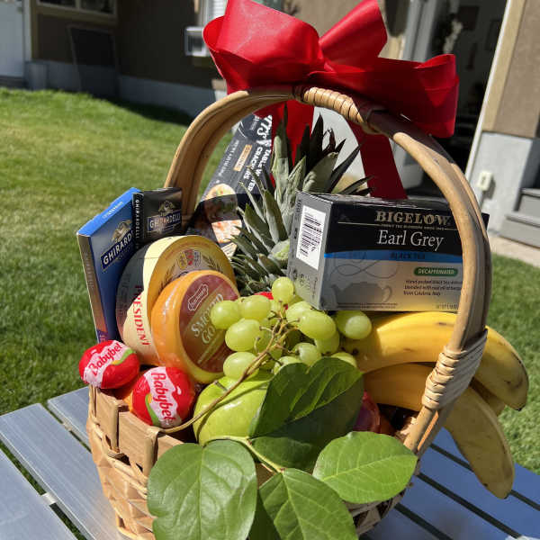 Gift basket with fruit, tea, cheese, and chocolates tied with a red bow