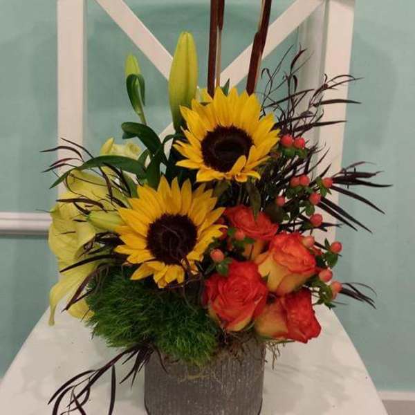 Sunflowers, roses, and lilies arranged in a gray vase