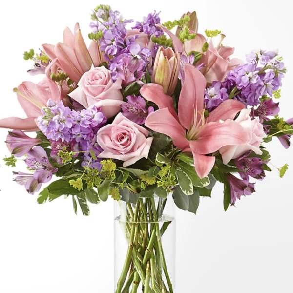 Pink lilies and roses arranged in a clear glass vase with purple flowers