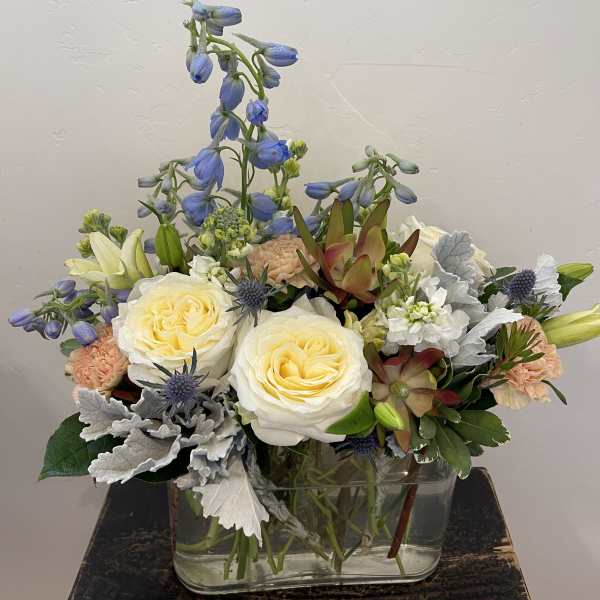 Mixed bouquet in a clear glass vase with cream roses and blue flowers