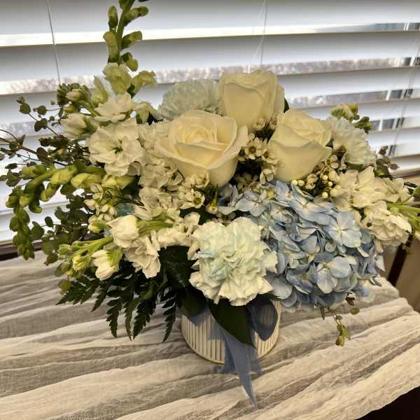 Low white and pale blue flower arrangement with roses and hydrangeas in a white vase