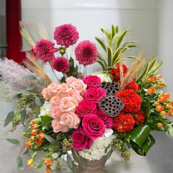 Mixed floral arrangement in a pedestal vase with pink, peach, and orange blooms