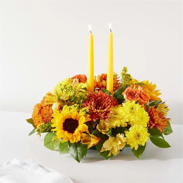 Yellow and orange floral centerpiece with two lit taper candles