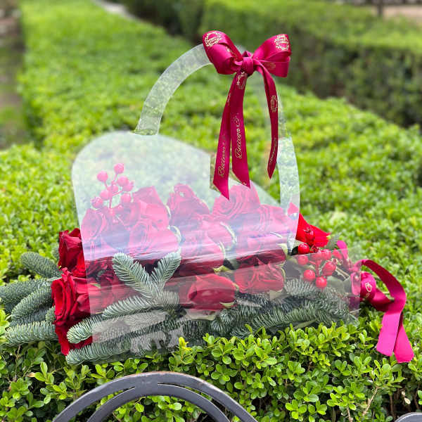 Red roses in a clear handled gift bag with a pink ribbon bow