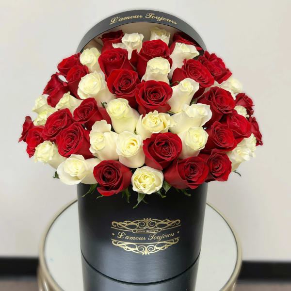 Round hatbox arrangement of red and white roses in a black box on a small table