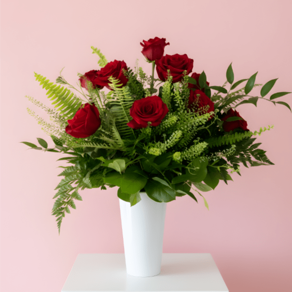 Red roses arranged in a white vase with green foliage