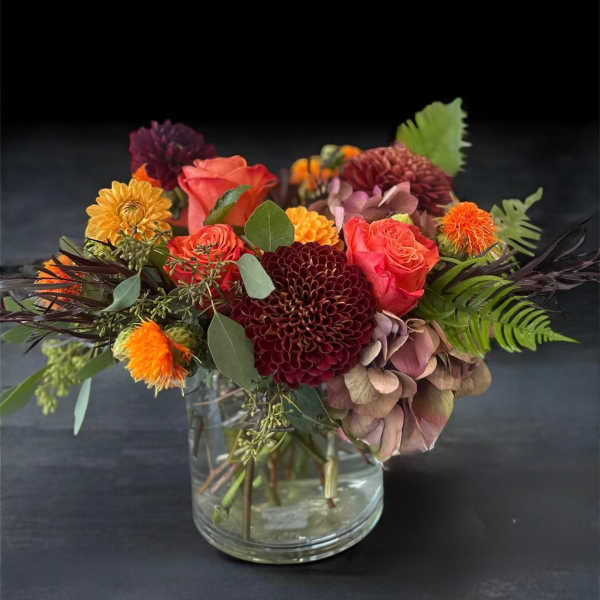 Mixed bouquet of orange, burgundy, and pink flowers in a clear glass vase