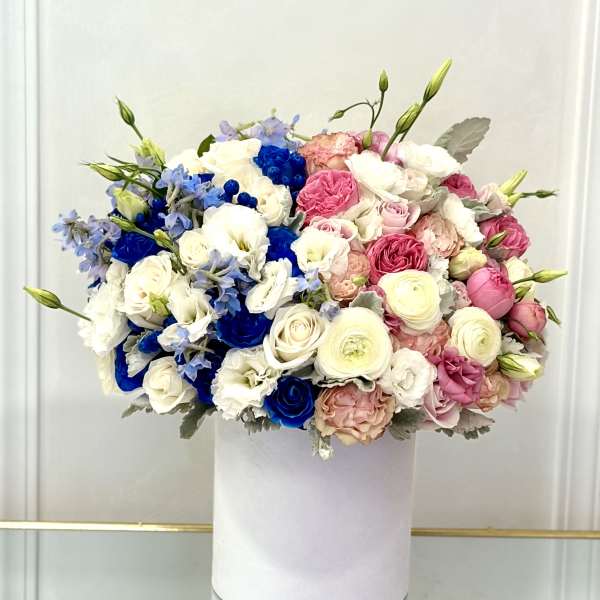 Round bouquet of pink, white, and blue flowers in a white box