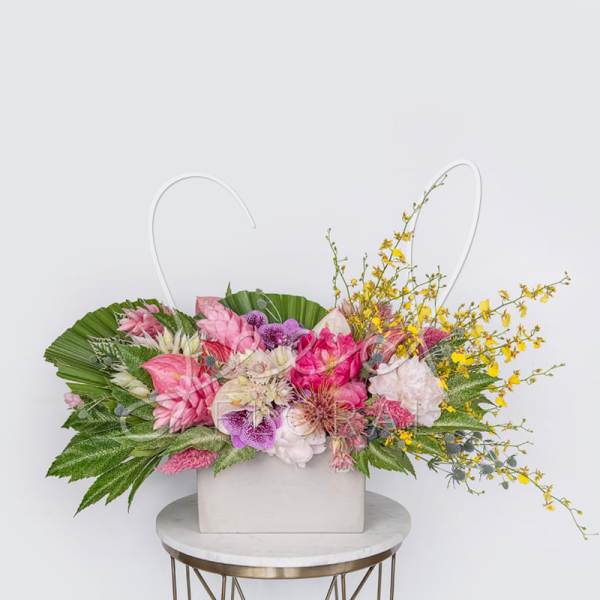 Wide tropical arrangement of pink, white, and yellow flowers in a low rectangular white container.