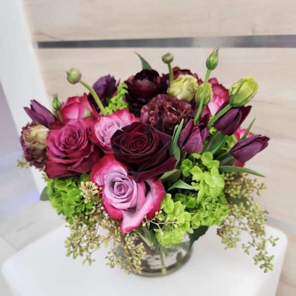 Compact bouquet of pink and burgundy roses with purple tulips and green hydrangeas in a glass vase