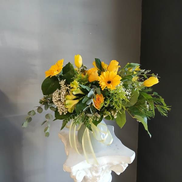 Yellow flower arrangement in a white vase with ribbon