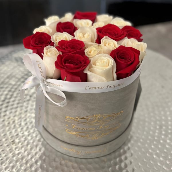 Round box of red and white roses arranged tightly in a gray hatbox with white printed ribbon.