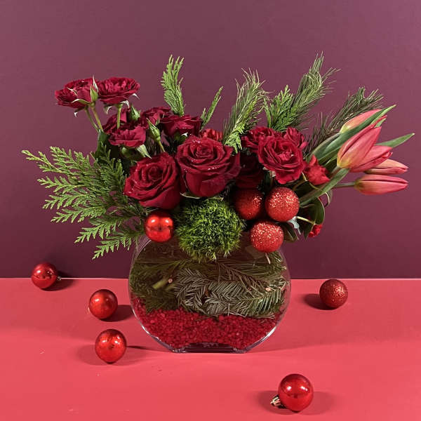 Red roses and pink tulips in a glass vase with holiday ornaments