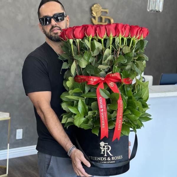 Man holding a large box of red roses with a red ribbon