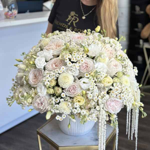 Large pastel bouquet of roses and white filler flowers in a white vase