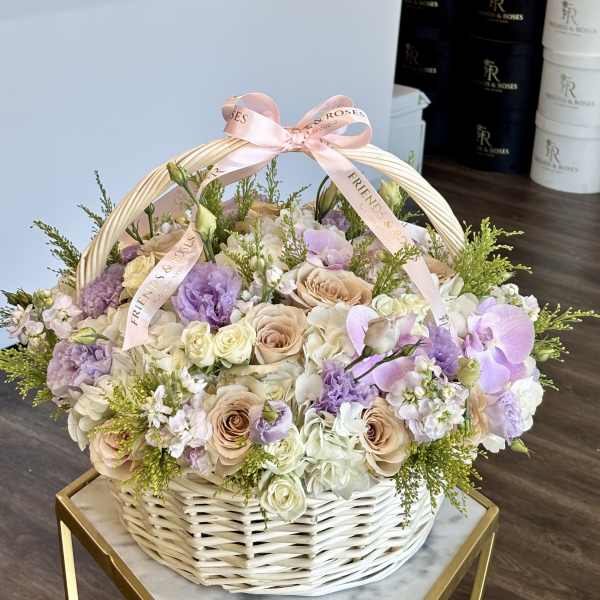 Pastel roses and orchids arranged in a white wicker basket with a pink ribbon