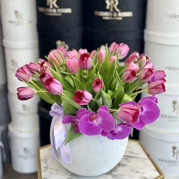 Pink tulips and purple orchids arranged in a round white vase