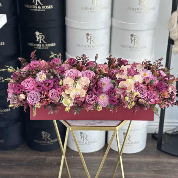 Long pink floral arrangement in a rectangular box on a gold stand
