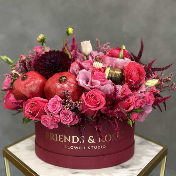 Pink and burgundy flower arrangement in a round box with pomegranates